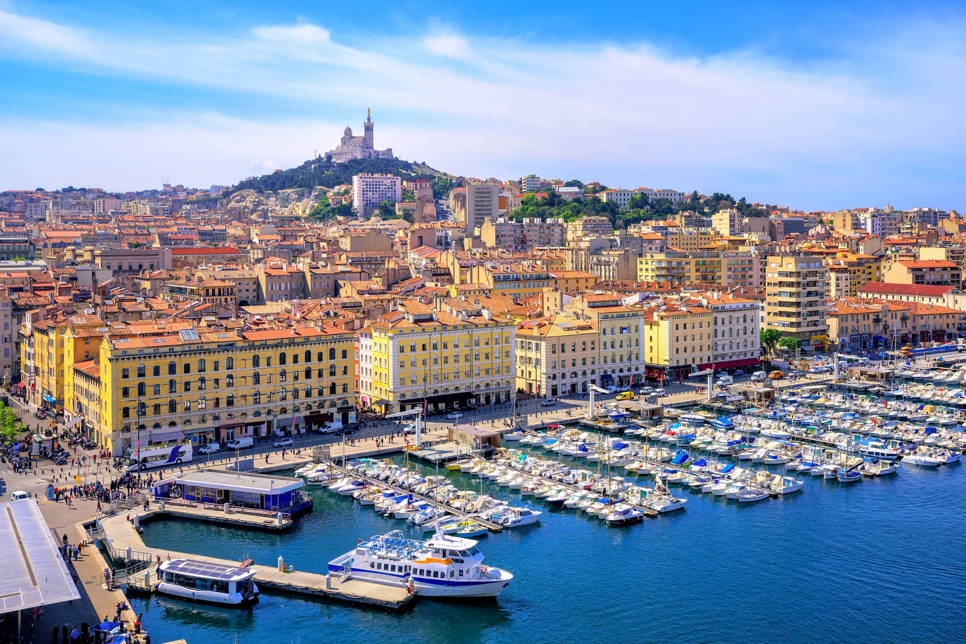 Vieux-Port Marselha, na parte inferior barcos atracados na marina. Na parte central predios amarelos, e ao fundo um castelo