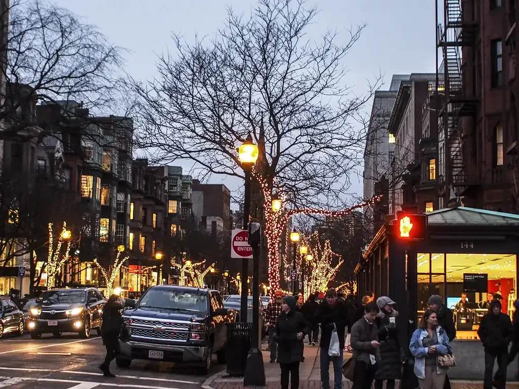 Movimentada Newbury Street em Boston durante o inverno, com luzes de Natal decorando as árvores e pedestres desfrutando das lojas e do clima festivo.