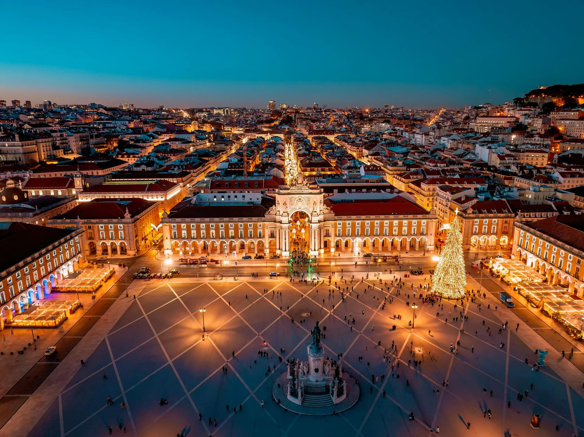 Vista aérea da Praça do Comércio em Lisboa, com iluminação natalina e o Arco da Rua Augusta ao centro, com a cidade iluminada ao fundo.