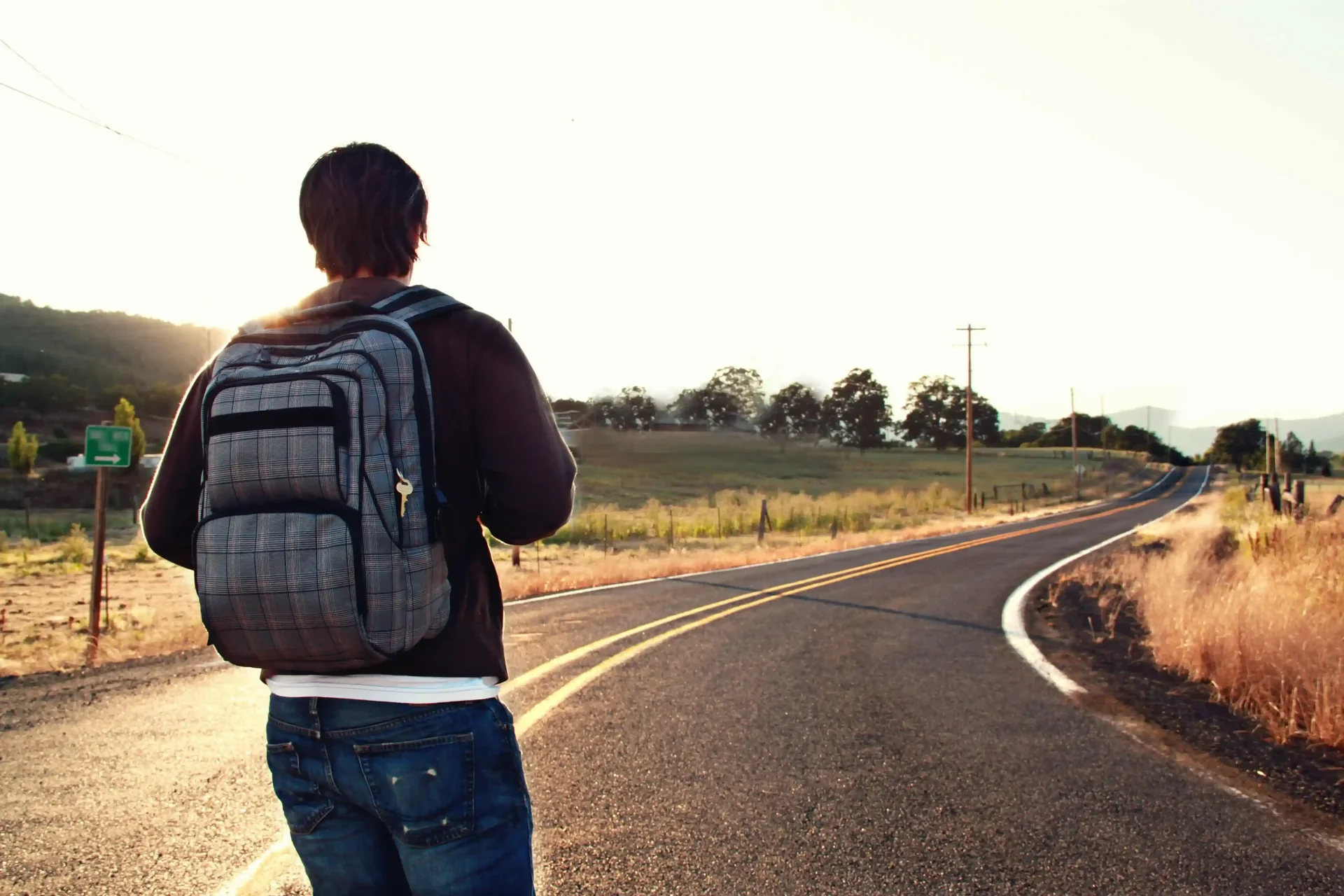 Homem com mochila em uma estrada curva olhando o horizonte.