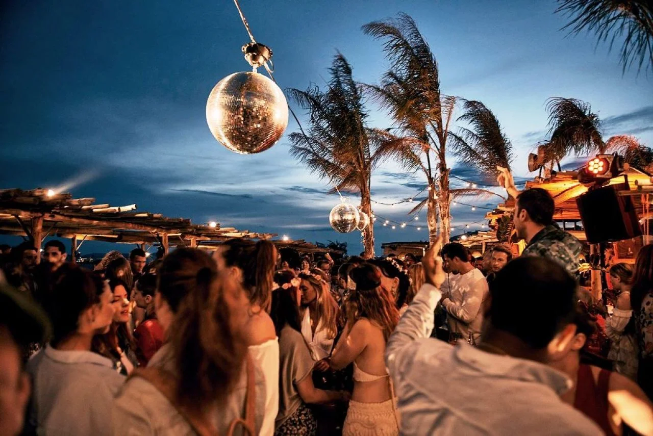 Pessoas dançando em festa no fim de tarde, com globos de espelho pendurados