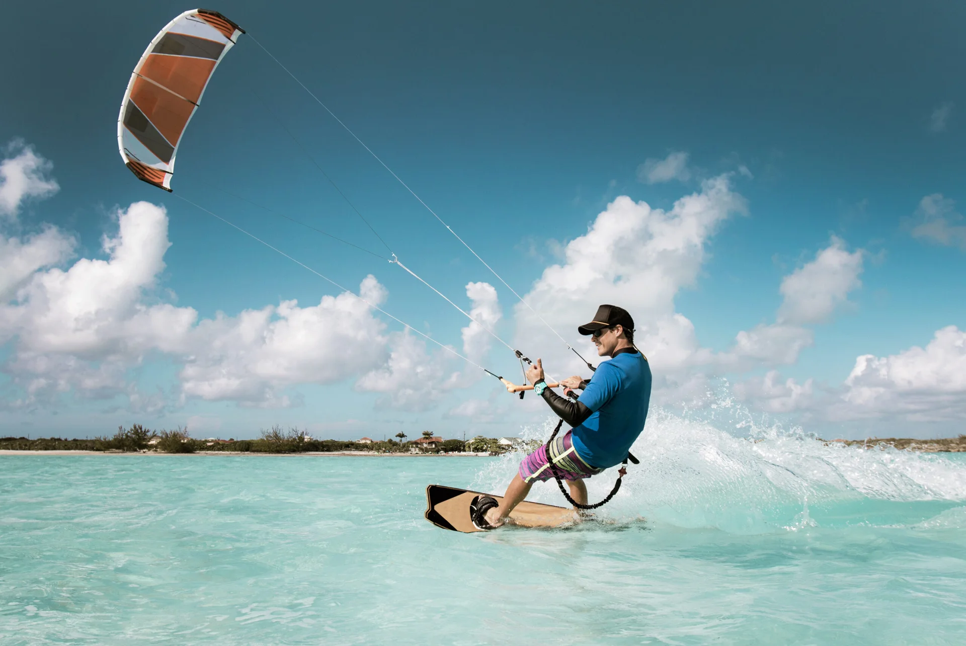 homem fazendo kitesurf em praia, com mar azul cristalino e seu azul com nuvens brancas
