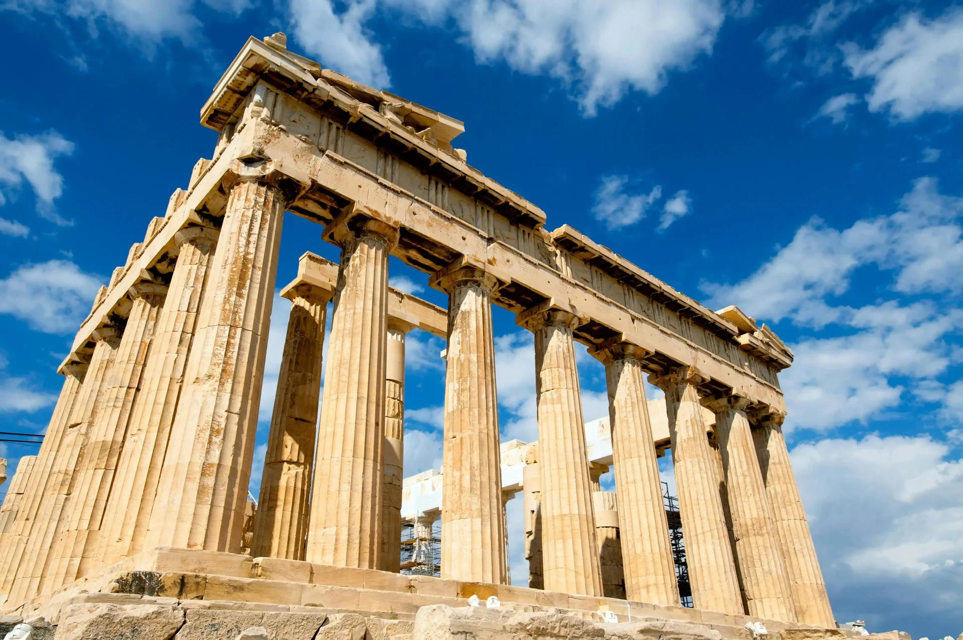Vista do Partenon em Atenas, Grécia, com suas colunas de mármore dourado sob um céu azul com nuvens esparsas.