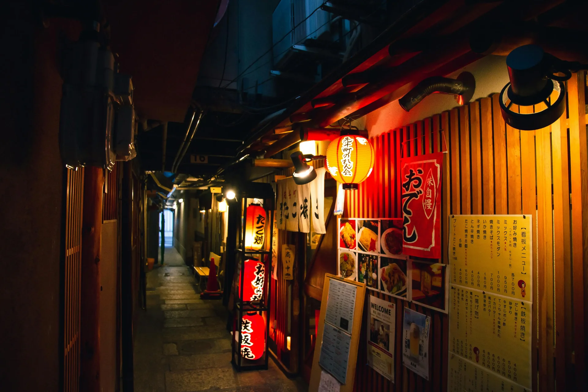 Rua estreita em Kyoto, Japão, à noite, com letreiros de restaurantes e lanternas japonesas iluminadas.