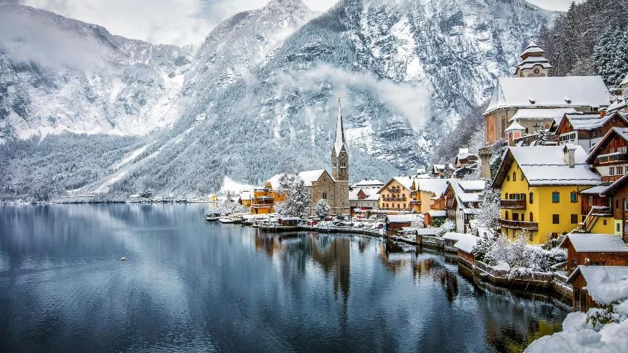 lago com uma vila do lado direito, coberta de neve e montanhas ao fundo