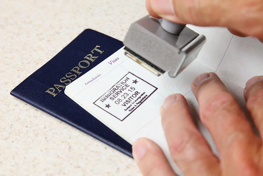 Carimbo de imigração sendo aplicado em um passaporte, ilustrando a etapa de entrada nos EUA.
