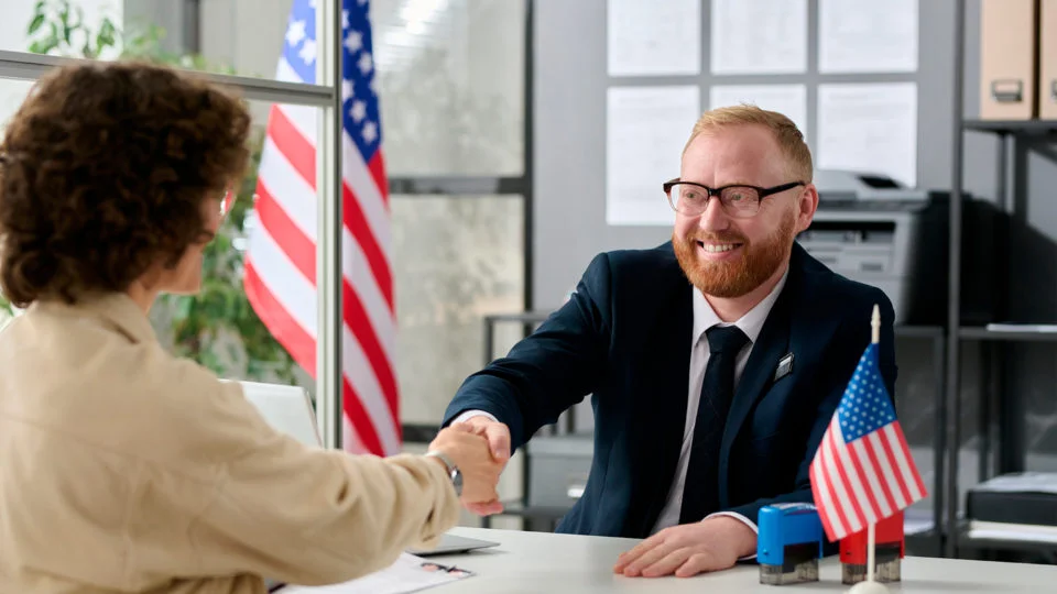 Pessoa apertando as mãos de um funcionário consular em um ambiente formal, representando a entrevista para o visto americano.