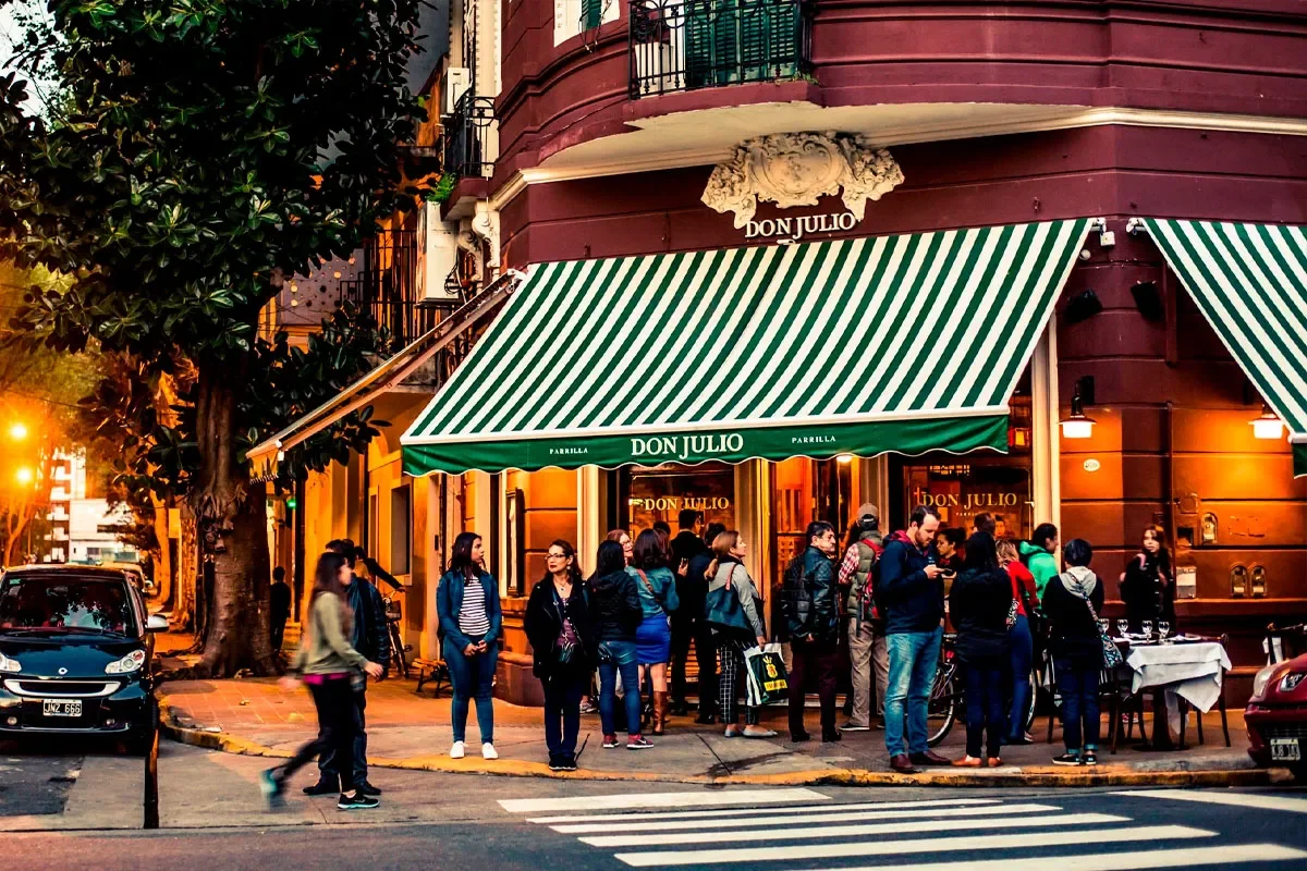 Fachada do restaurante Don Julio em Buenos Aires, com pessoas reunidas na entrada e toldo verde e branco destacado.