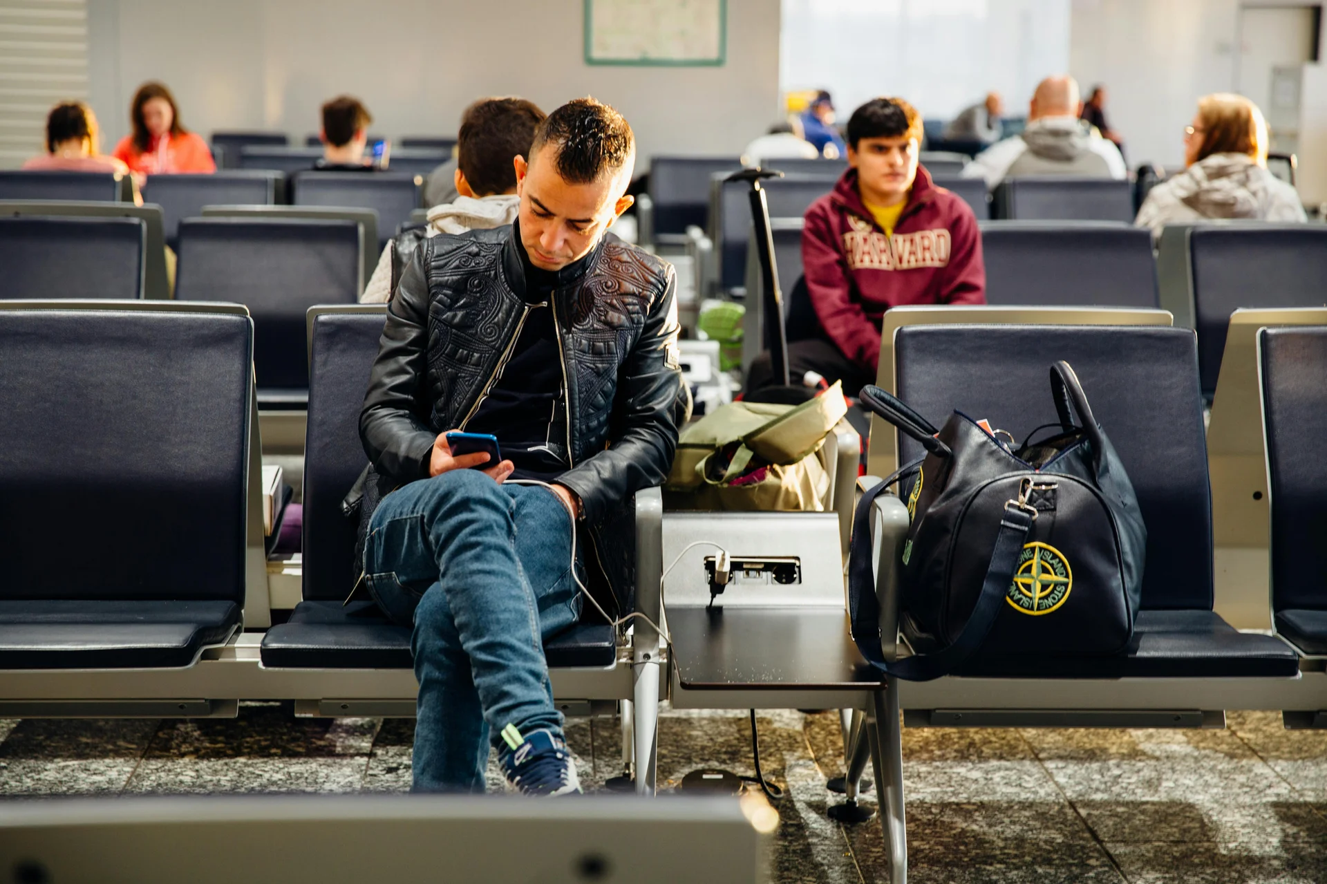 Homem sentado em cadeira de aeroporto conferindo documentos digitais em seu smartphone.
